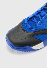 Blauer Sportschuh mit einem schwarzen Lederspitze, Mesh-Obermaterial und perforierten Details. Enthält blaue Schnürsenkel und eine strukturierte Sohle.