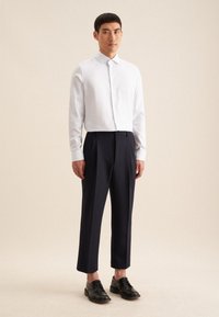 Wit gestreepte overhemd met knopen en een puntige kraag, gecombineerd met marineblauwe tapered broek. Zwarte leren schoenen maken de outfit compleet.