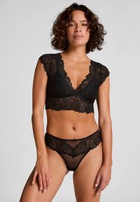 Črni modrček iz čipke z valovitimi robovi in kratkimi rokavi; ujemajoče se prosojne boke s pikami in čipkastim robom. Zapletena cvetlična zasnova.