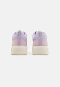 Lila sneakers áttetsző dizájnnal, párnázott sarokkal és vastag fehér talppal. A hátul található logó címke a részletekért felel.