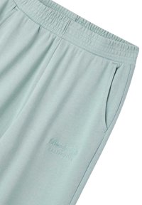 Pantaloni della tuta azzurri con cintura elastica, tasca laterale e testo ricamato "Beverly Hills California" sulla coscia.