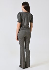 Top a motivi in bianco e nero con maniche a sbuffo corte, abbinato a pantaloni aderenti a zampa. Tessuto liscio, dettagli hardware minimal.