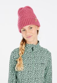 Berretto a maglia di colore rosa antico con righe texturizzate e punta in alto. Il modello indossa una maglietta con colletto a zip di colore verde menta con un motivo a macchie nere.