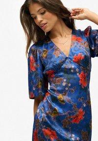 Blauwe bloemen wikkeljurk met korte pofmouwen, levendige rode en oranje bloemen, en een gladde, glanzende stoftextuur.