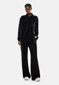 Giacca camicia in velluto nero con un sottile motivo leopardato, dotata di colletto, tasche frontali e maniche lunghe, abbinata a pantaloni neri a gamba larga.