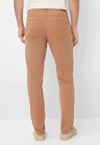 Lichbruin katoenen broek met een rechte pijpdesign, vijf zakken en zichtbare stiksels. Draag met lichtgekleurde schoenen.
