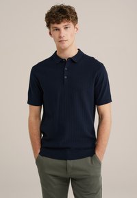 Polo de manga corta en color navy con un patrón texturizado y acanalado. Presenta un dobladillo recto, tres botones y un collar plano. Se lleva con pantalones verdes claros.