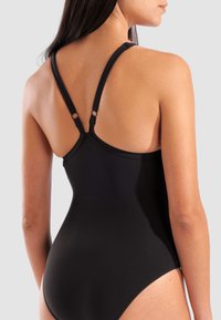 Le maillot de bain une pièce noir présente une texture lisse, des bretelles réglables avec des détails en métal et un design épuré.