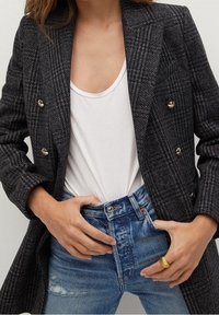Dwurzędowa szara marynarka w kratę houndstooth z metalowymi guzikami, zestawiona z białą bluzką i zniszczonymi niebieskimi dżinsami o wysokim stanie.