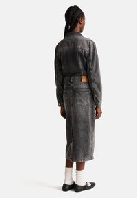 Abito in denim nero sbiadito con maniche lunghe, spacco posteriore e tasca applicata. Presenta cuciture a contrasto e un'etichetta sulla fascia posteriore.