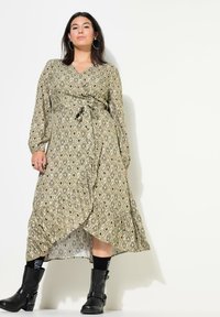 Un vestido largo de envoltura con un diseño de diamante en verde oliva, que presenta mangas largas, una cintura con lazo y un dobladillo con volantes. Combinado con botas negras.