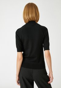 Sort kortærmet sweater med en tætsiddende silhuet, ribbet kant og glat tekstur. Båret med stribede bukser. Bagansigt vist.