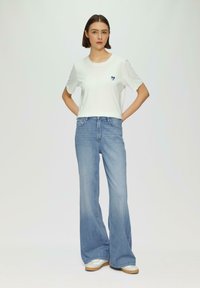 White short-sleeve t-shirt with a small navy heart graphic, paired with light blue flared jeans and silver sneakers.