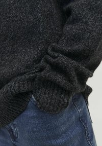 Pull en tricot gris foncé avec des poignets et un bas côtelés. La texture est douce, avec une coupe ample au niveau de la taille. Porté avec un denim bleu.