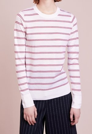 Camisa blanca de manga larga con rayas horizontales rojas, cuello redondo y puños acanalados, combinada con pantalones oscuros de rayas.