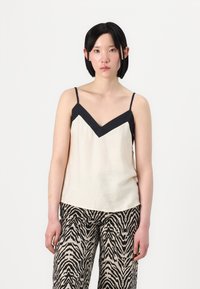 Camiseta de tirantes crema con un inserto negro en forma de V, tirantes delgados y textura suave, combinada con pantalones de pierna ancha en estampado de cebra negro y beige.