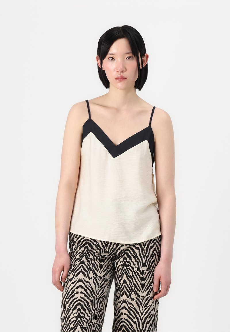 Camiseta de tirantes crema con un inserto negro en forma de V, tirantes delgados y textura suave, combinada con pantalones de pierna ancha en estampado de cebra negro y beige.