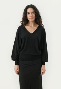 Maglione nero con scollatura a V, maniche lunghe e un design testurizzato caratterizzato da strass sparsi. Abbinato a una gonna nera aderente.