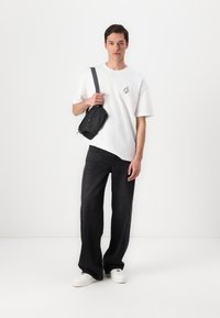 Black crossbody bag, white oversized t-shirt with logo, dark jeans, and white sneakers. Minimalist design with contrasting colors and textures.