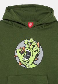 Sweatshirt verde com uma ilustração de uma mão a gritar dentro de um design circular. Feito de tecido macio, com um bolso frontal e cintura em ribana.