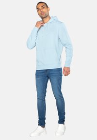 Světle modrá mikina s klokaní kapsou, kapucí na šňůrku a žebrovanými manžetami, spárovaná s tmavě modrými úzkými džíny a bílými teniskami.