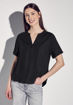 Černý krátký rukáv top s V- výstřihem, hladkým povrchem a ohrnutými rukávy, kombinovaný se světlými šedými džíny. Minimalistický design.