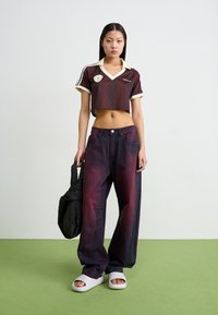 Dark red cropped polo shirt with a pattern, white collar; loose purple jeans, white slide sandals; carries a black puffer bag.