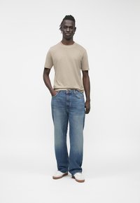 Tricou bej cu mâneci scurte, asortat cu blugi din denim albastru deschis, cu picioare largi, și adidași albi. Textură netedă, fără modele vizibile.