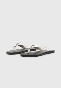 Infradito argentate con una tomaia metallica e suola in gomma nera. Presentano un design a flip-flop con cinturini incrociati e plantare testurizzato.