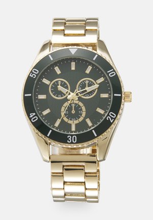 Gulltonet armbåndsur med svart urskive, tre subskiver og gullakenter. Har en metall lenkebånd og en teksturert bezel.