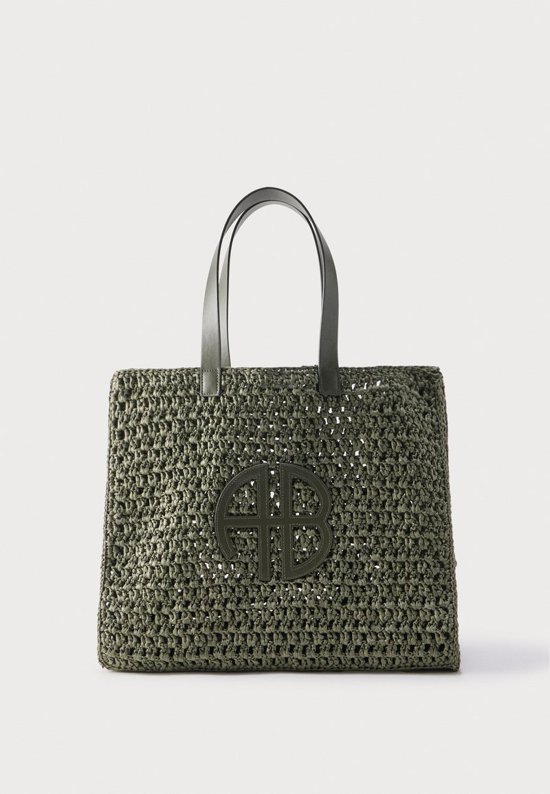 Green knitted tote bag with double leather handles and circular leather logo patch on front.