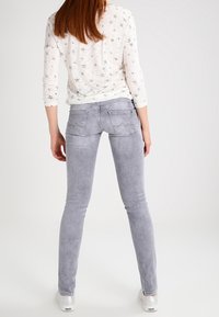 Světle šedé skinny džíny s hladkou texturou, se zadními kapsami s prošívanými detaily, nošené s bílým dlouhým rukávem s motivem hvězd.