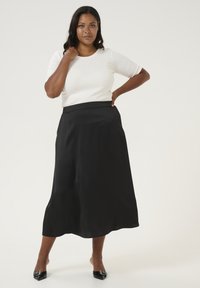 Zwarte A-lijn rok met een gladde textuur, hoge taille en vloeiende ontwerp. Combinatie met een aansluitend wit topje en zwarte puntige schoenen.