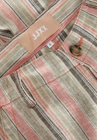 Gestreepte stof met roze, goud en zwarte lijnen. Heeft een kleine bruine knoop en een merklabel met "JJXX" maat "S." Gestructureerd materiaal.
