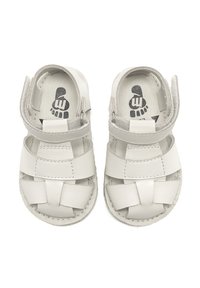 Sandalias de cuero blancas con un diseño abierto, que cuentan con tiras trenzadas, cierre de velcro y suelas de goma. Interior impreso con un gráfico de huella.