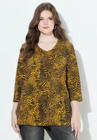Mustat ja keltaiset V-pääntiellä varustettu toppi, jossa on rohkea eläinkuosimalli ja kolmannen neljänneksen hihat, valmistettu kevyestä kankaasta.