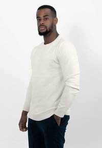 Crème-kleurige longsleeve sweater met een ronde hals en geribbelde manchetten, gecombineerd met donkere broek. Soepele textuur, casual pasvorm.