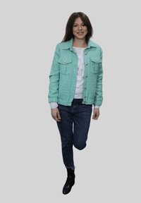 Chaqueta texturizada verde menta con dos bolsillos delanteros, cierre de botones, usada sobre una blusa blanca con volantes y combinada con jeans oscuros y botas negras.