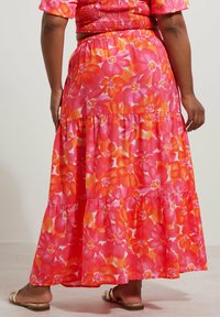 Jupe maxi florale avec un design à volants dans des tons vibrants de rose et d'orange, confectionnée en tissu léger avec une texture douce.