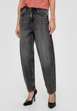 Kobieta ubrana w wyblakłe czarne jeansy z wysokim stanem i prostą nogawką, zestawione z czarnymi szpilkami z szpiczastym noskiem oraz włożonym do środka koralowym topem.