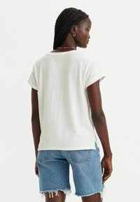 Biała koszulka z krótkim rękawem z podwiniętymi mankietami, luźny krój i bocznymi rozcięciami, zestawiona z niebieskimi szortami dżinsowymi z postrzępionym dołem.