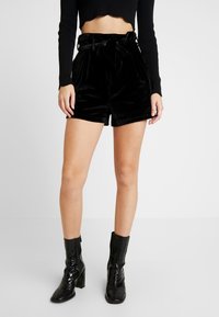 Sammetsliknande högmidjade svarta shorts med knytband i midjan, i kombination med blanka svarta klackboots med ankeldesign och reptilmönster.