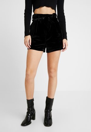 Sammetsliknande högmidjade svarta shorts med knytband i midjan, i kombination med blanka svarta klackboots med ankeldesign och reptilmönster.