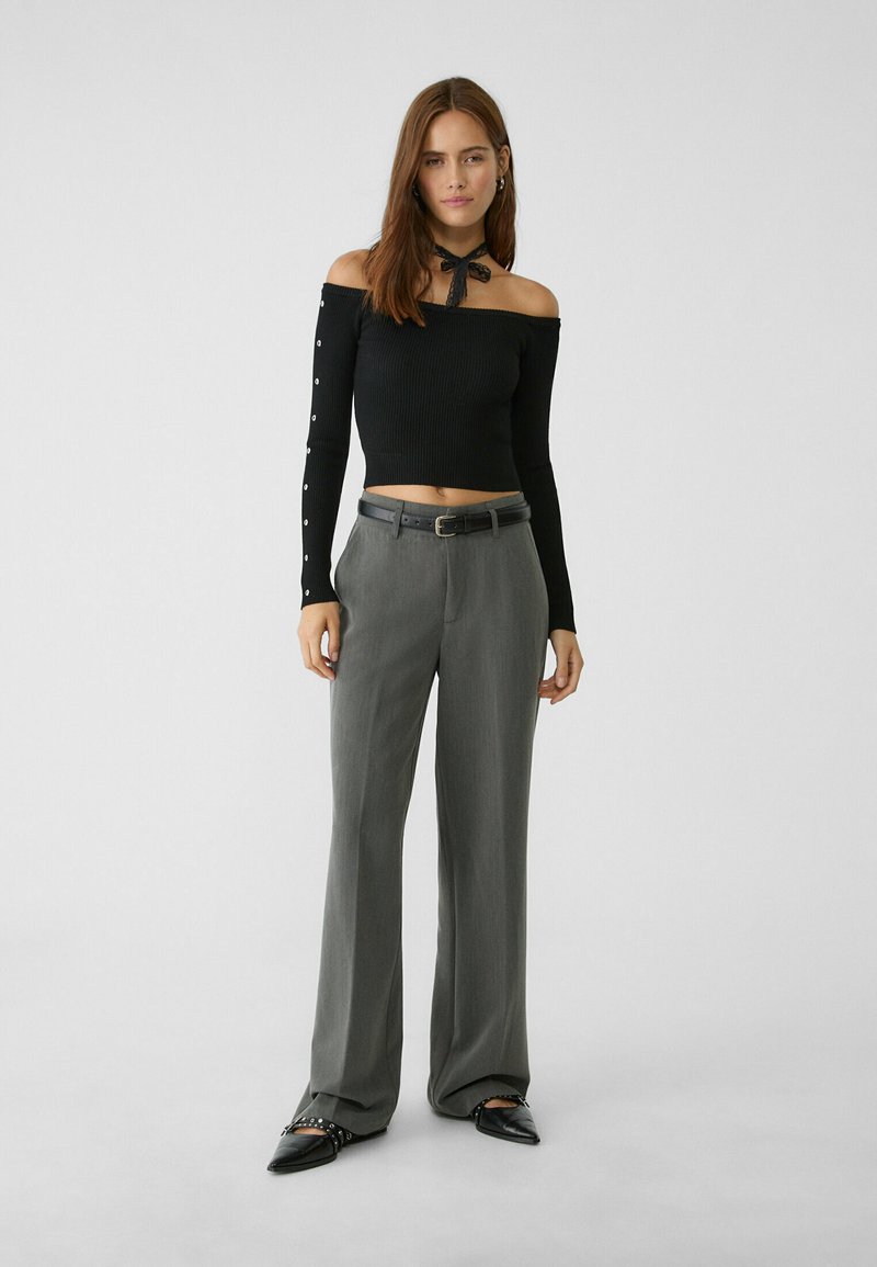 Haut court noir à côtes à épaules dénudées avec des manches longues, ornée de boutons, associée à un pantalon taillé gris clair et des ballerines noires à bout pointu.