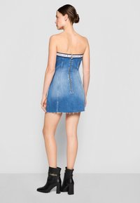 Strapless denim dress in light blue with a zip closure at the back and frayed hem. Paired with black heeled ankle boots and gold accents.