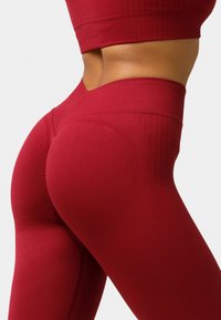Red athletic leggings with a textured waistband, featuring ribbed detailing and a contoured design for shape enhancement.