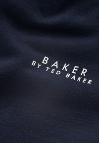 Laivastonsininen kangas, jossa on teksturoitu kudos ja valkoinen "BAKER by TED BAKER" -logo. Yksinkertainen muotoilu ilman lisäkuvioita tai kiinnikkeitä.