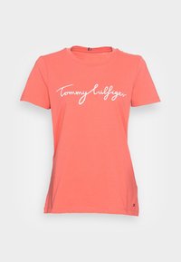 Koralowa, krótko rękawowa koszulka damska z okrągłym dekoltem oraz białym logo "Tommy Hilfiger" na piersi.