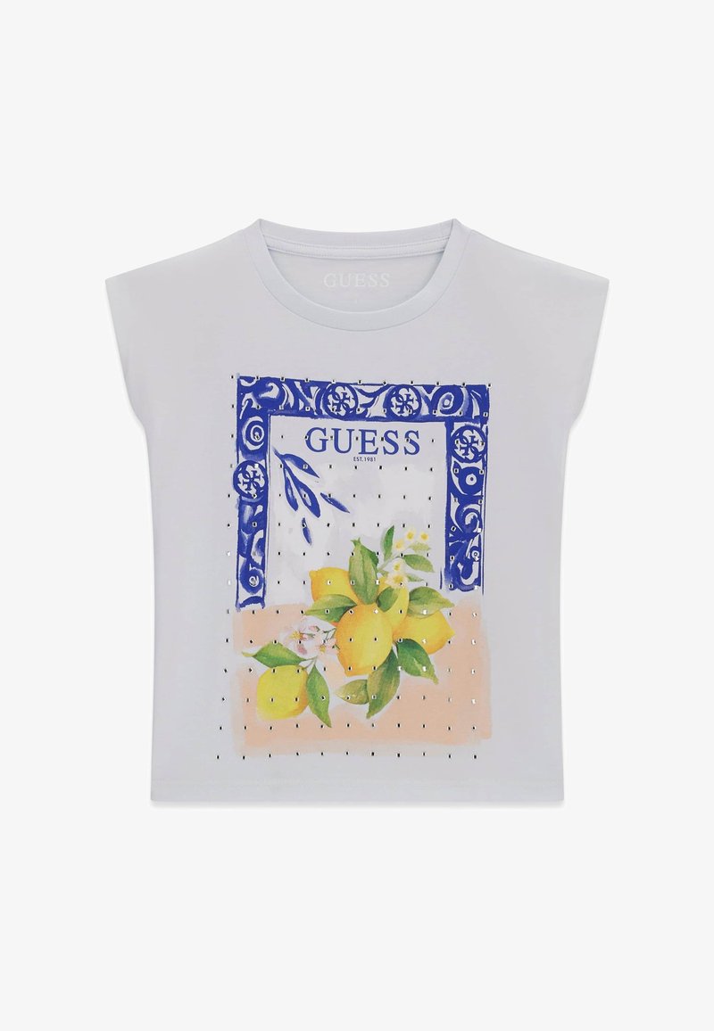 Chemise blanche sans manches avec un cadre ornemental bleu, le texte "GUESS" et un groupe de citrons jaunes avec des feuilles vertes à l'avant.