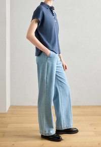 Polo shirt navy à manches courtes, avec deux boutons, associé à un jean taille haute de couleur bleu clair et des chaussures noires. Design minimaliste et décontracté.